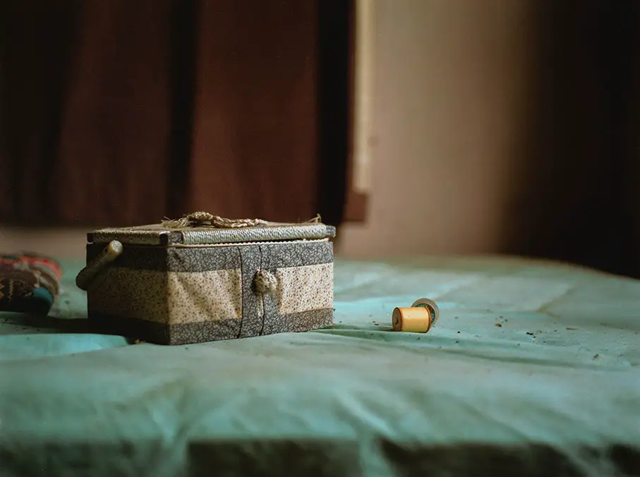 A patterned fabric box with a braided handle and a yellow spool of thread rest on a dusty teal surface.