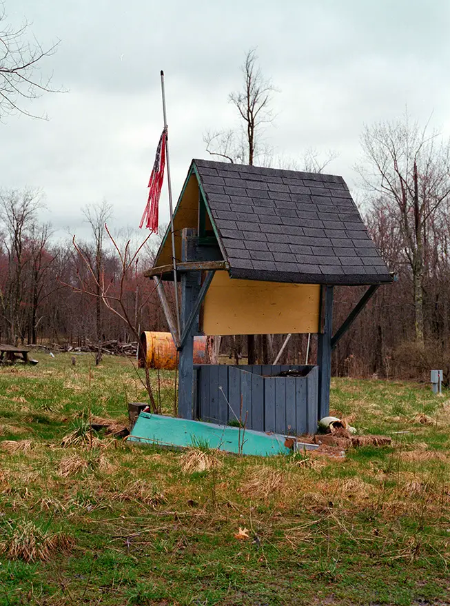 Weathered blue well structure with a tattered red and blue flag and blank sign at Lily of the Valley Campground, Ohio.