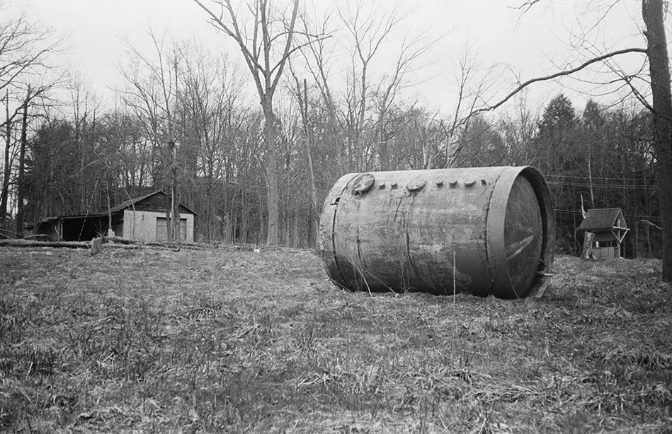 Rusted tank on bare ground, with abandoned structures and leafless trees at Lily of the Valley Campground, Thompson,