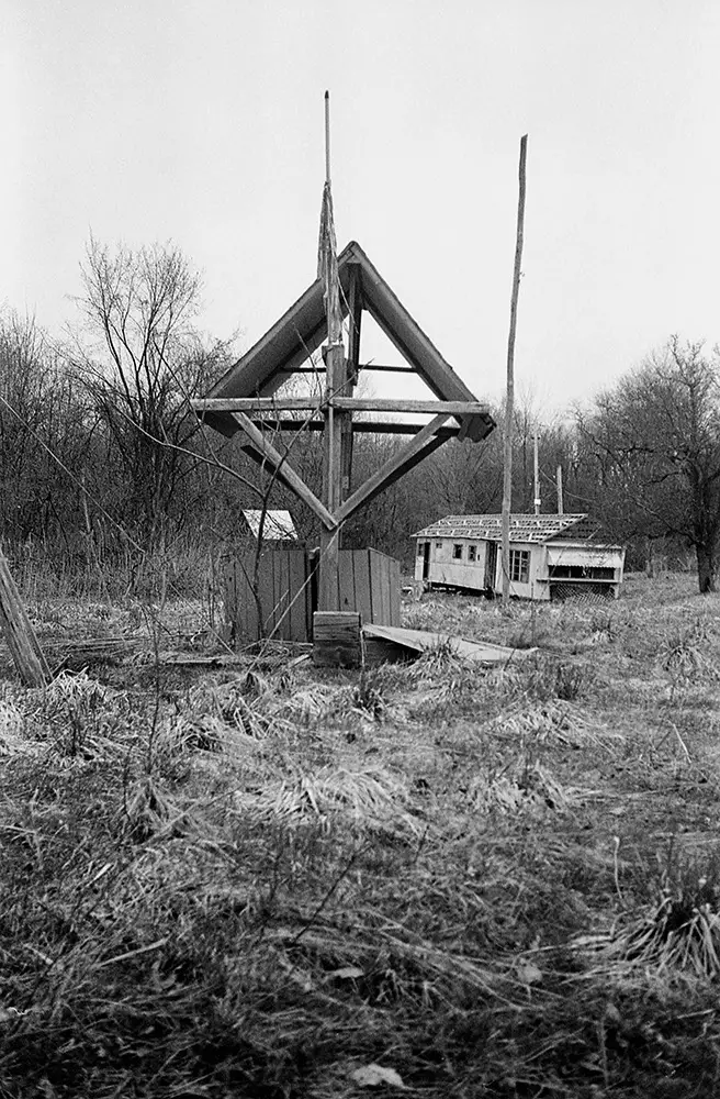 Monochrome view of Lily of the Valley Campground showing a weathered wooden arch and a decaying building in dry grass.